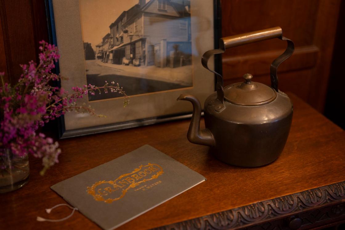 Photograph of a tea kettle, framed photo, flowers, and letter on a desk